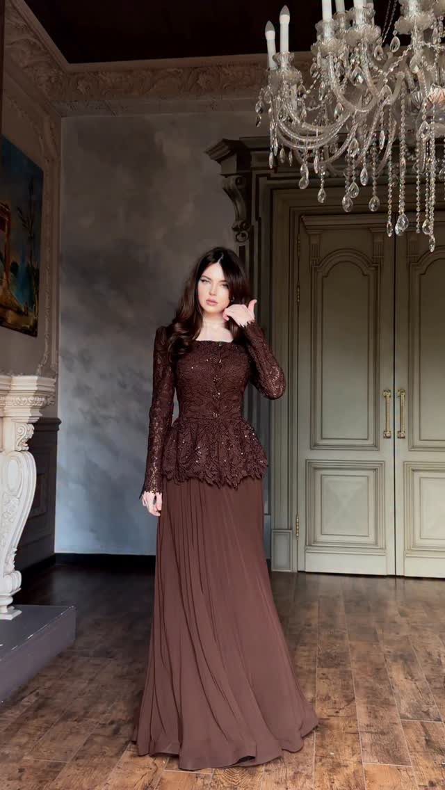 Woman wearing a long-sleeved brown lace bodice and a flowing pleated maxi skirt.