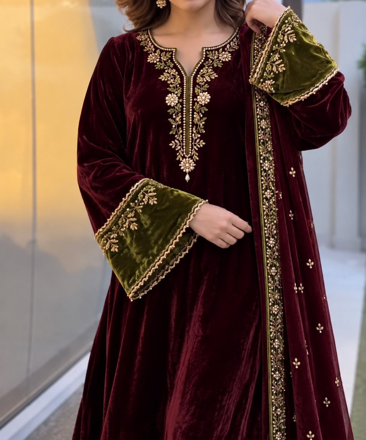 Person wearing a burgundy velvet dress with gold embroidery and green velvet cuffs.