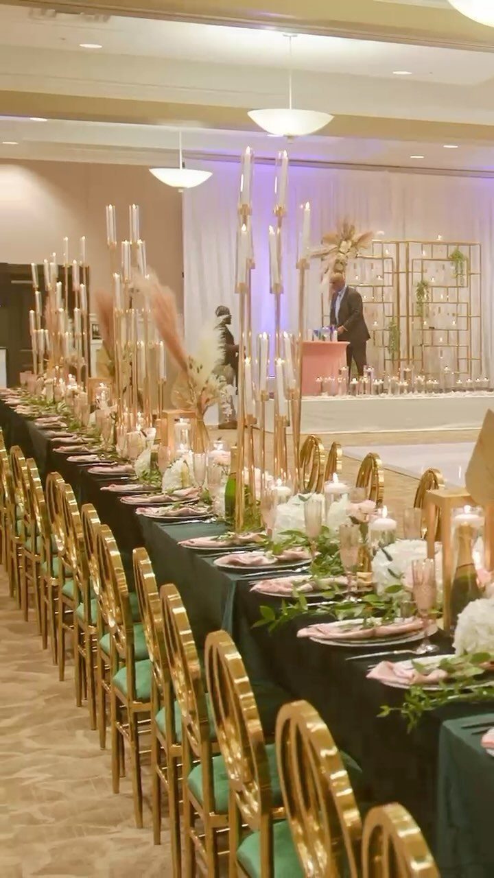 Long wedding reception table featuring emerald green linens, gold chairs, and blush pink floral accents.