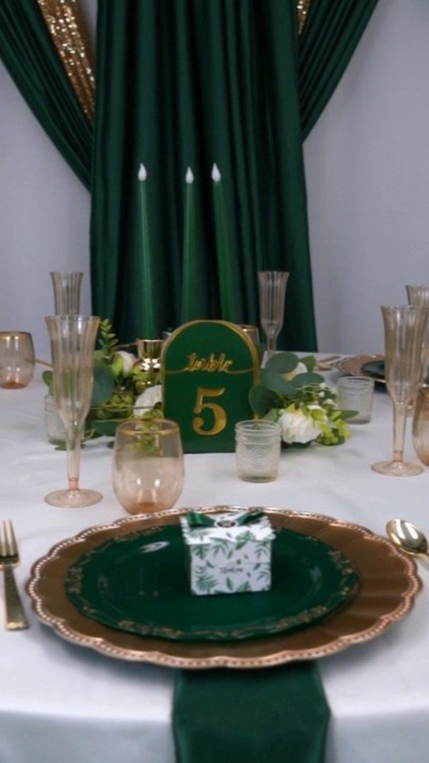 Emerald green plates and gold chargers set on a white wedding table with champagne flutes.