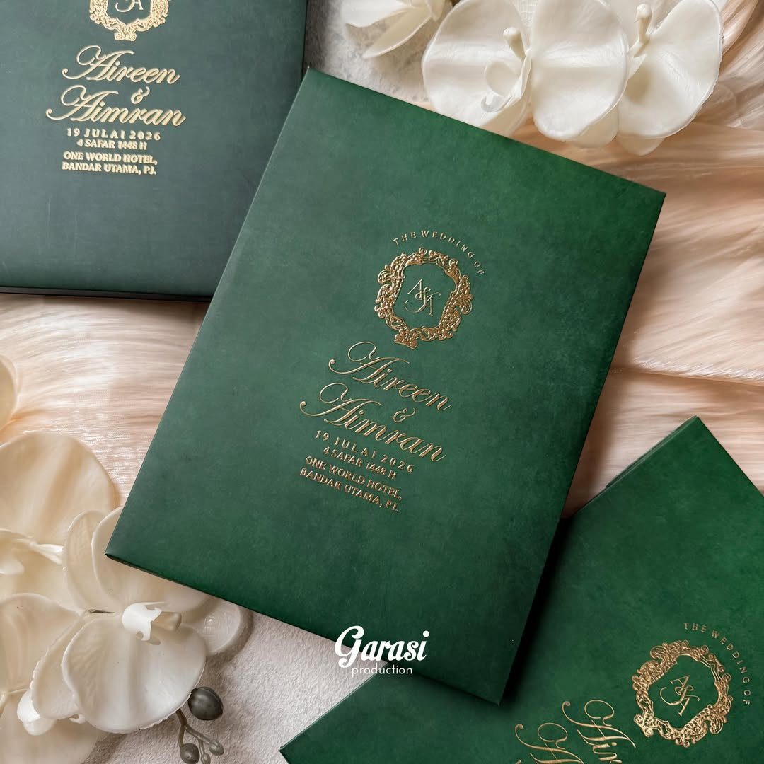 Emerald green wedding invitations with gold foil text and crests on pink fabric.