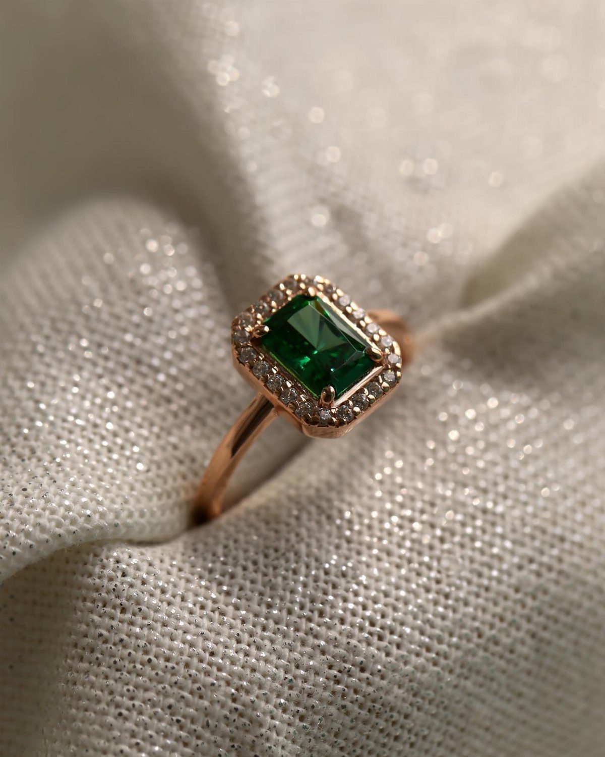 An emerald green gemstone ring set in rose gold on white fabric.