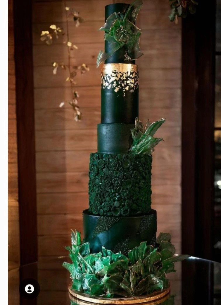 A tall emerald green wedding cake with gold leaf accents and green floral textures.