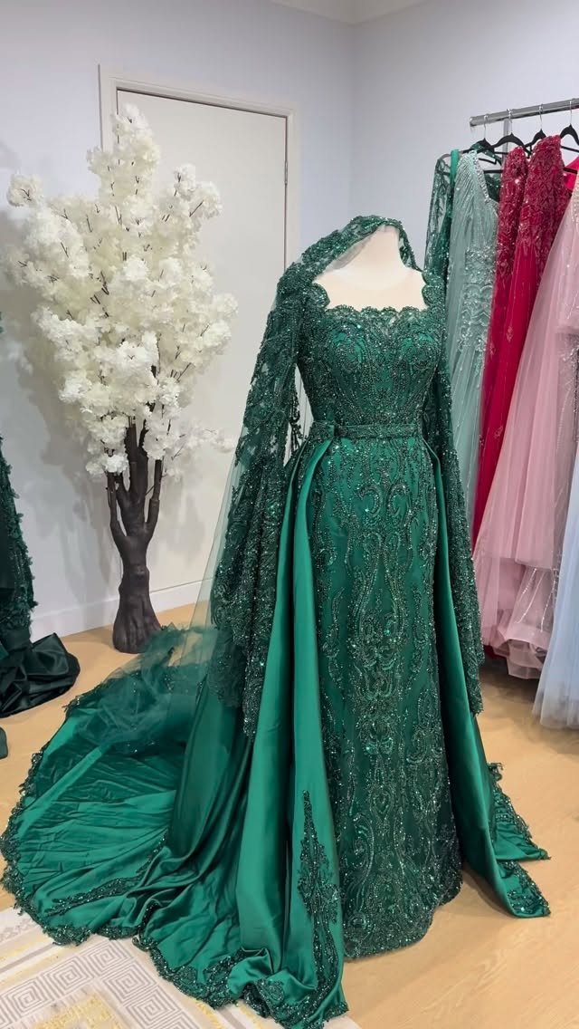 Emerald green lace wedding dress with long sleeves and a flowing train on a mannequin.