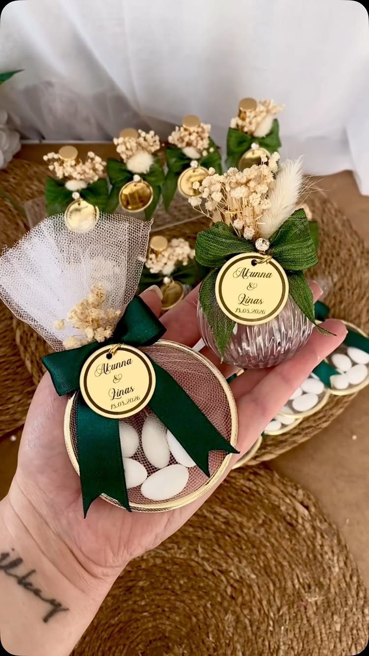 A hand holds round wedding favor containers filled with white candies and decorated with green ribbons.