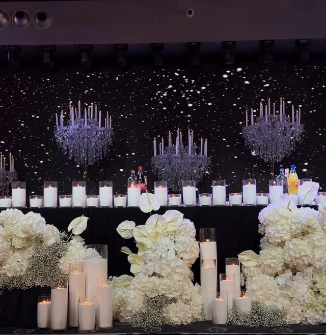 White candles and floral arrangements set against a black backdrop with sparkling lights.