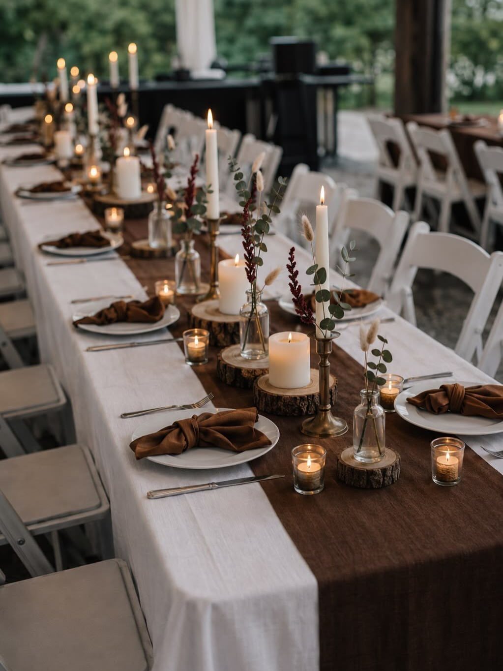 A long wedding reception table decorated with white linens, brown runners, and glowing candles.