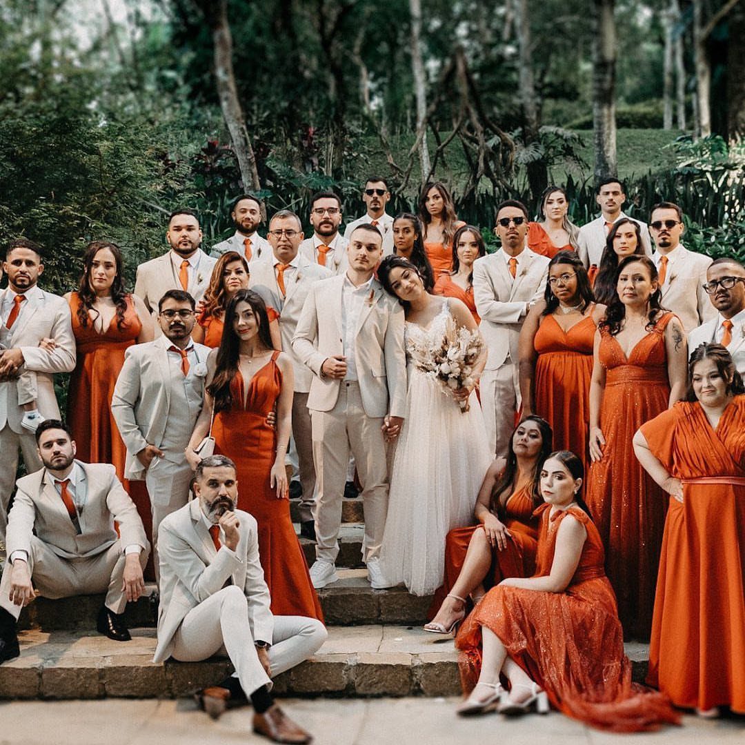 A wedding party posing in cream suits and terracotta dresses amidst a lush green forest background.