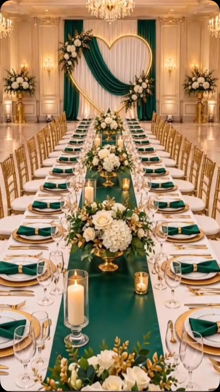 A long wedding banquet table decorated with emerald green runners, gold accents, and white floral arrangements.