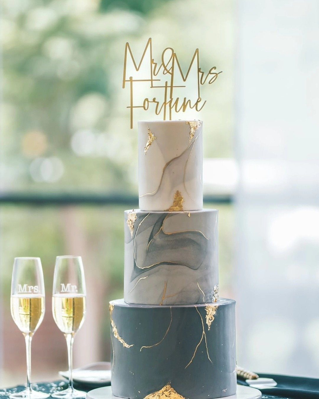 A three-tiered marble wedding cake decorated with gold leaf and a gold topper.