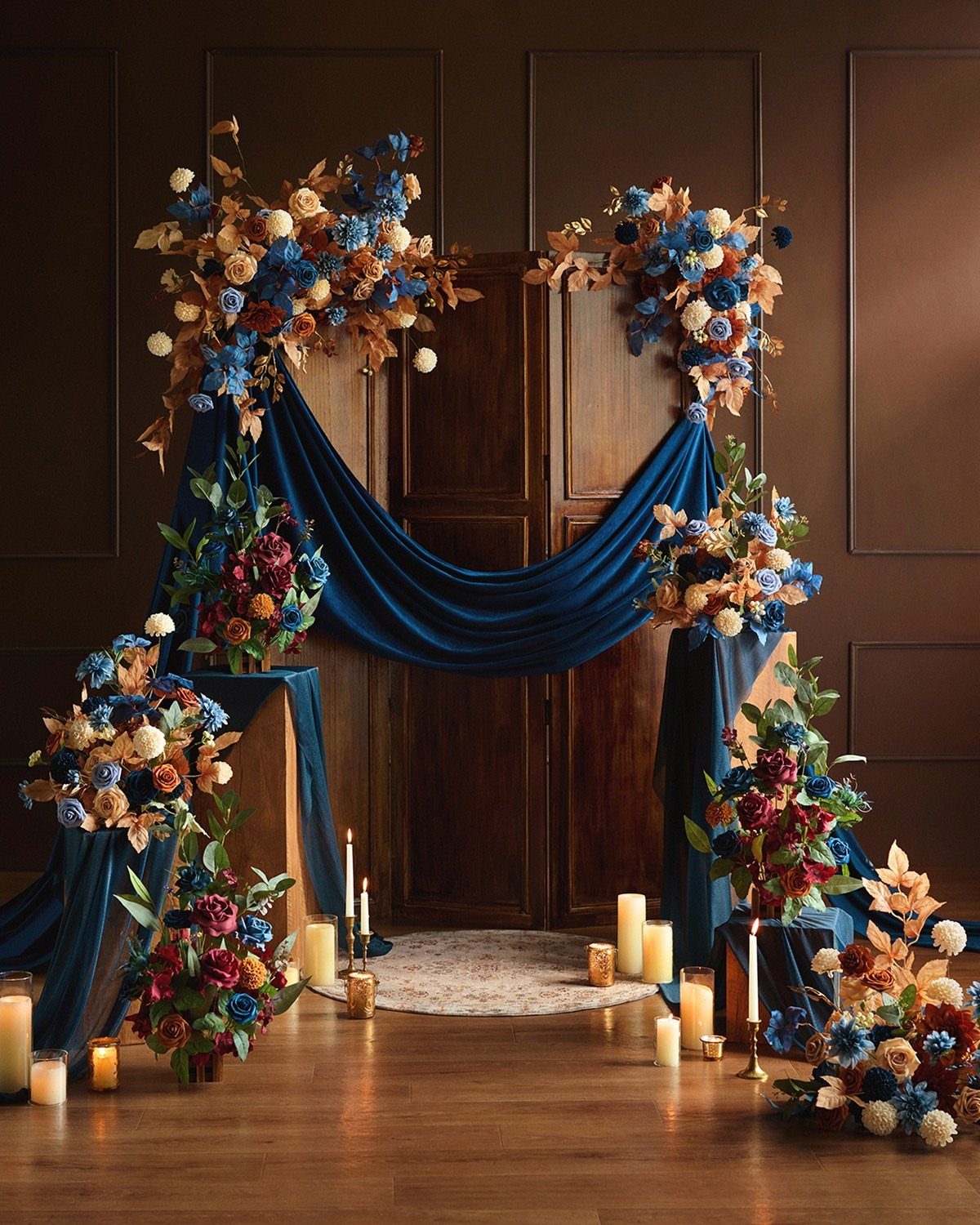 Blue velvet fabric draped over a wooden door surrounded by peach and blue floral arrangements and candles.