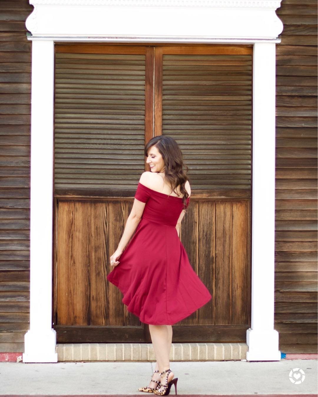 A woman in a burgundy off-the-shoulder midi dress posing in front of a wooden door.