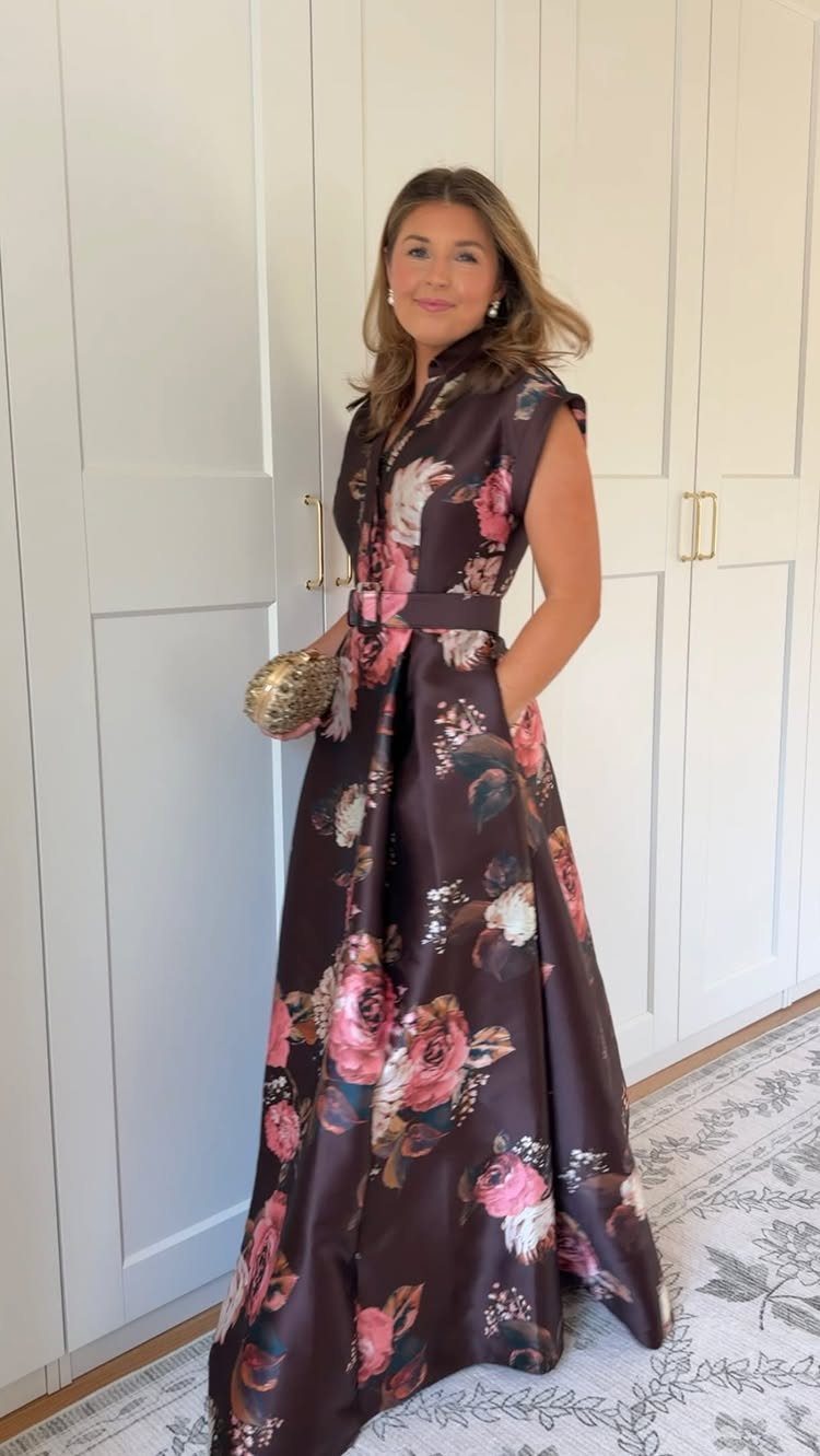 Woman wearing a long sleeveless floral maxi dress and holding a gold clutch.