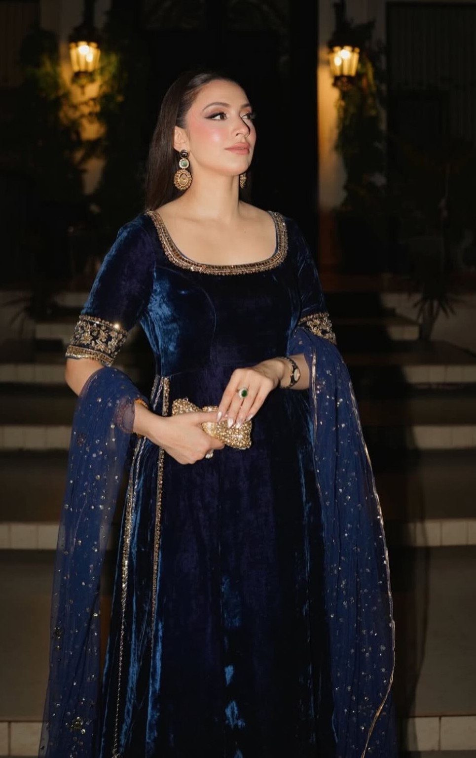 Woman in a navy blue velvet dress with gold embroidery posing outdoors at night.