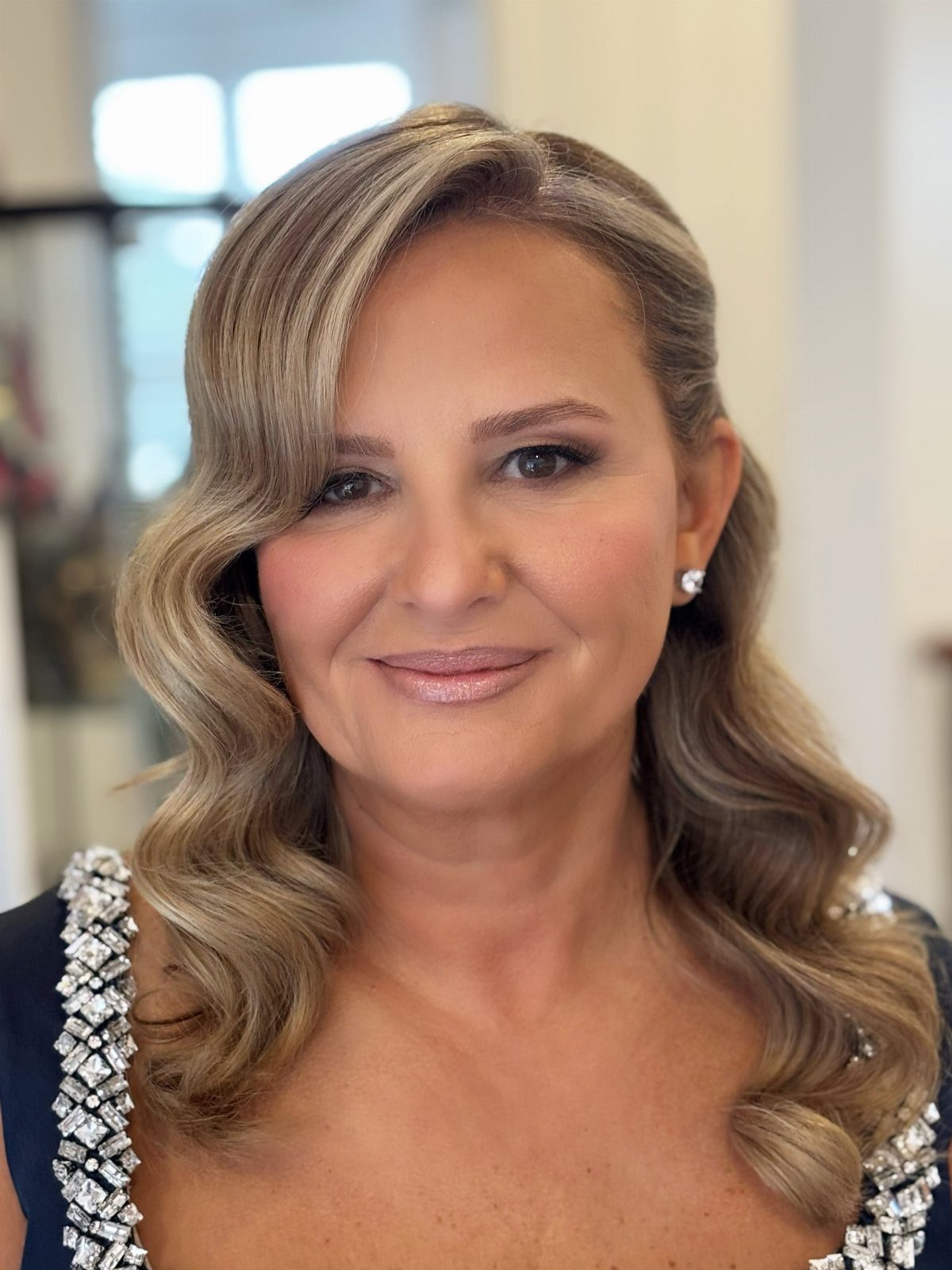 A woman with wavy blonde hair and polished makeup smiling at the camera.