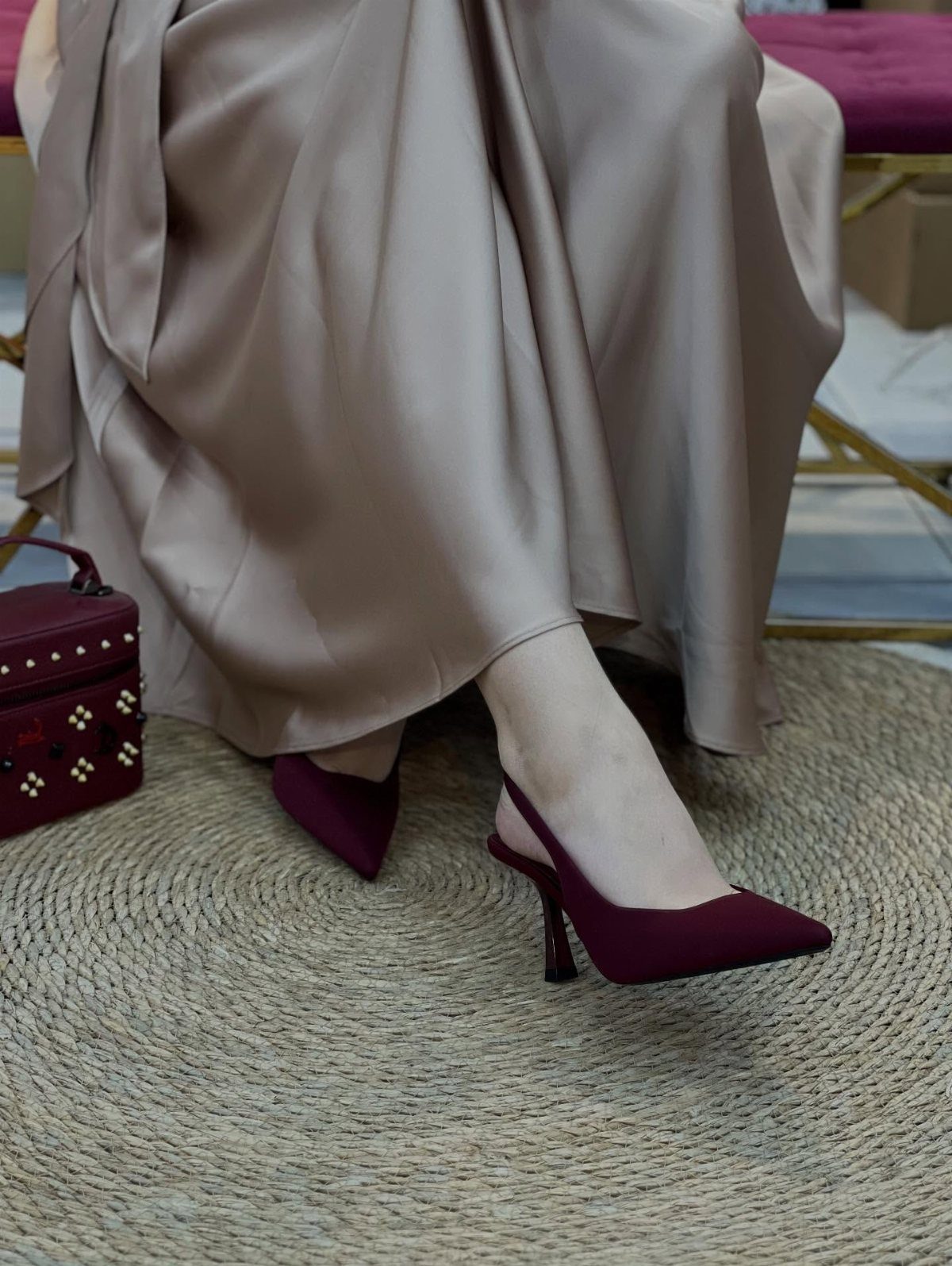 Burgundy stiletto pumps worn with a champagne satin gown on a woven rug.