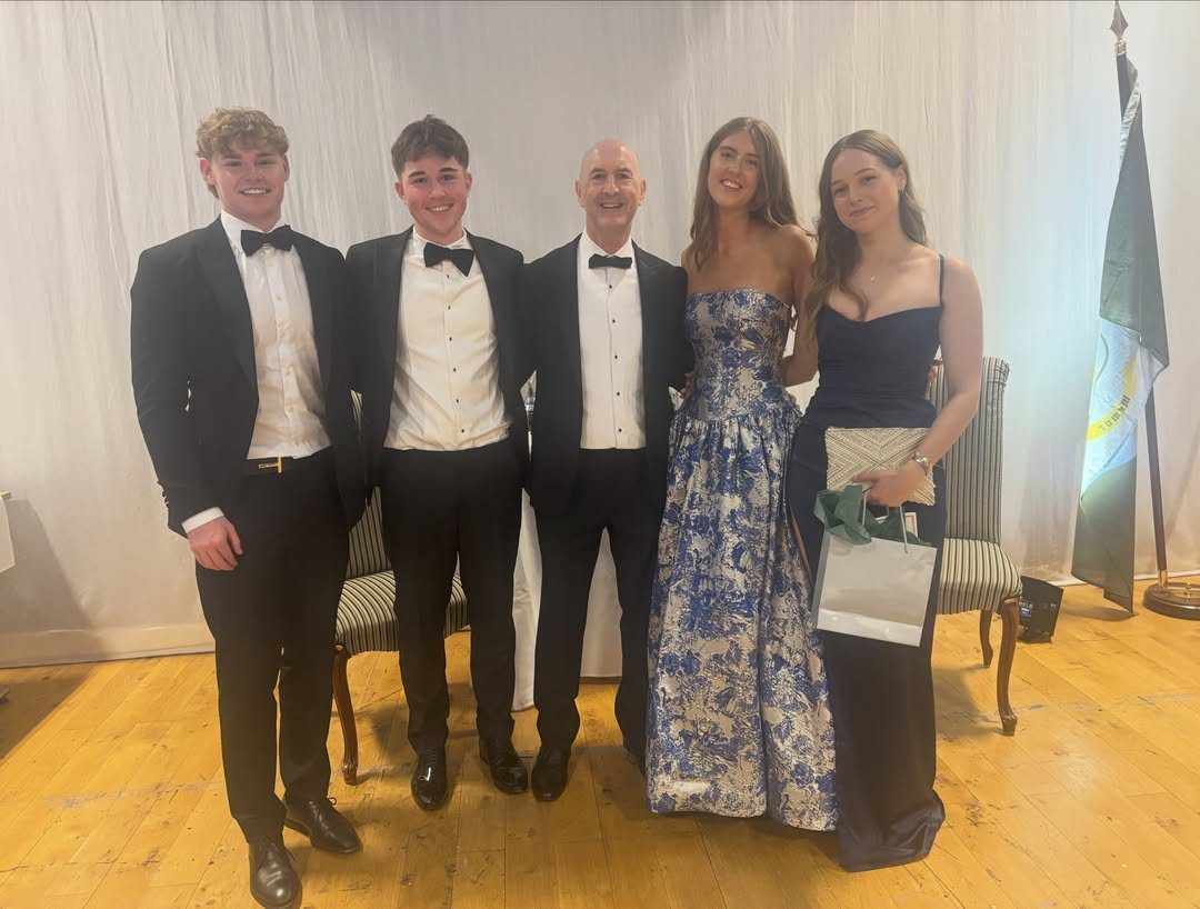 Five people posing in formal evening attire including tuxedos and long gowns.