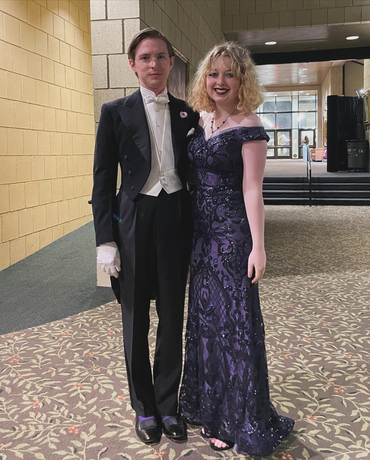 A young man in formal tailcoat and a woman in a purple evening gown posing together.