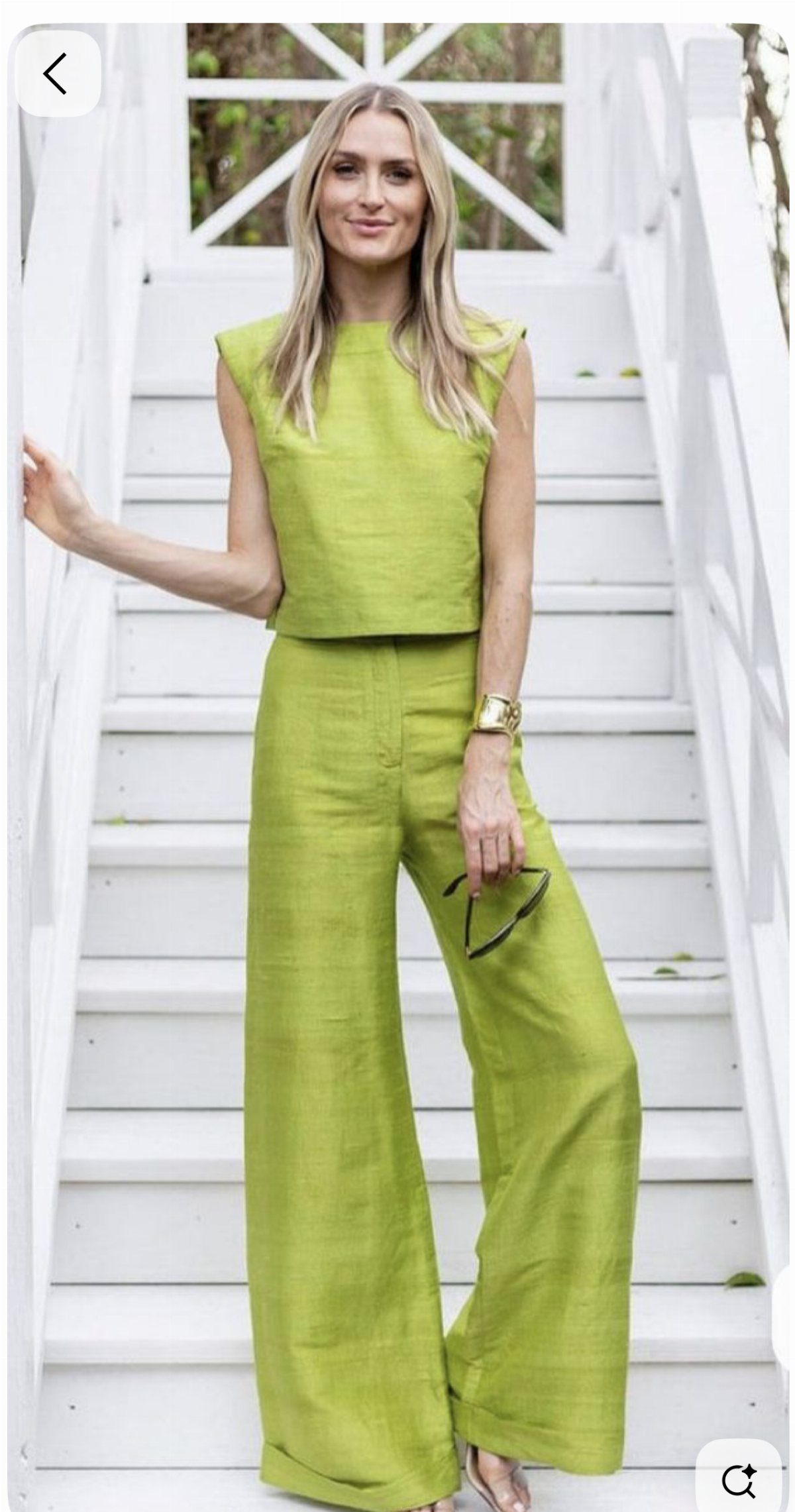Woman in a lime green sleeveless top and wide-leg trousers on white stairs.