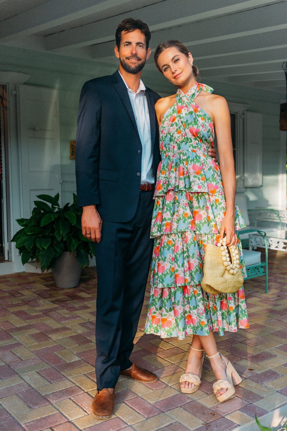 Man in navy suit and woman in floral dress posing on a porch.