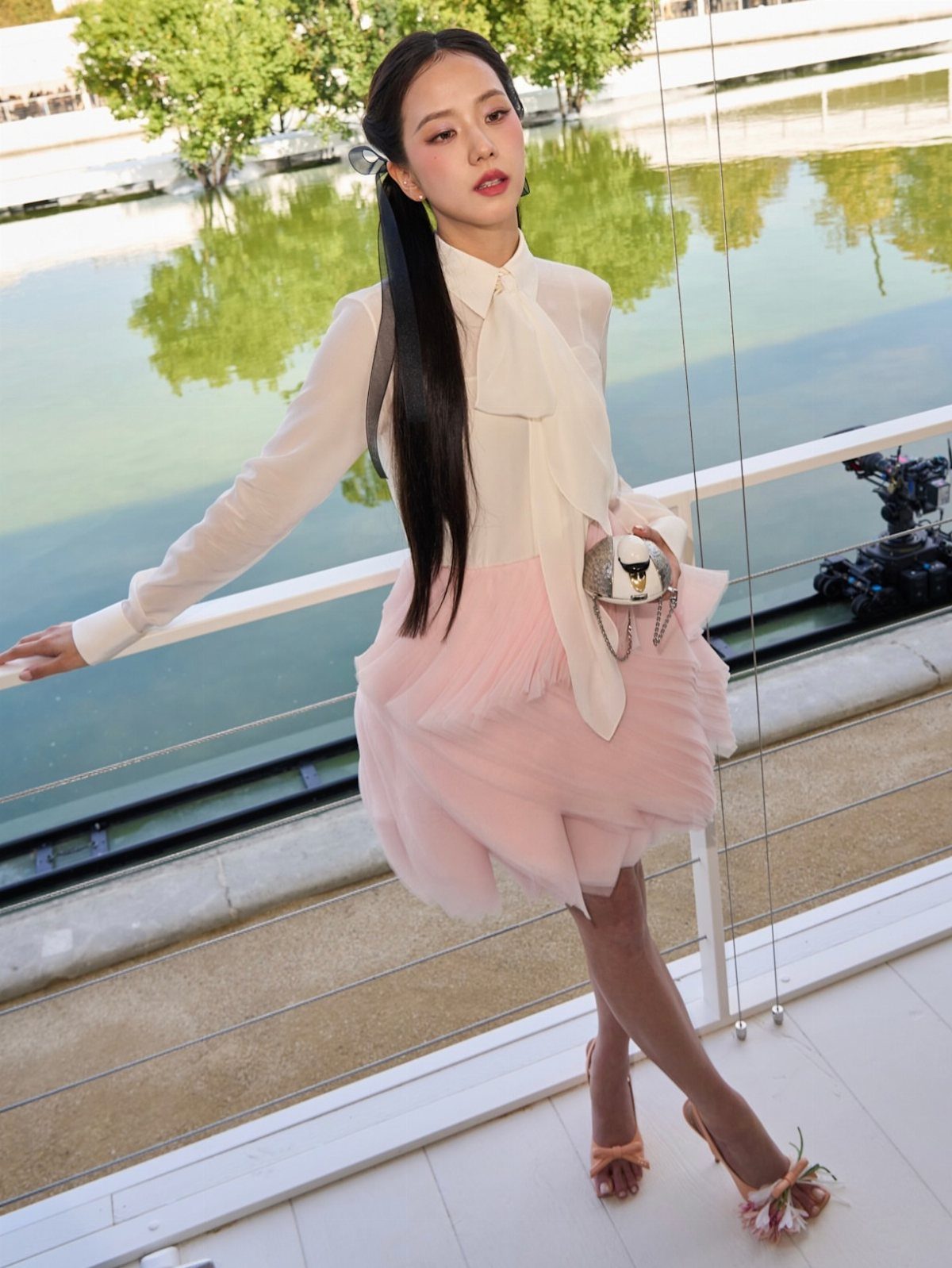 Woman in a white blouse and pink tulle skirt posing on a balcony near water.