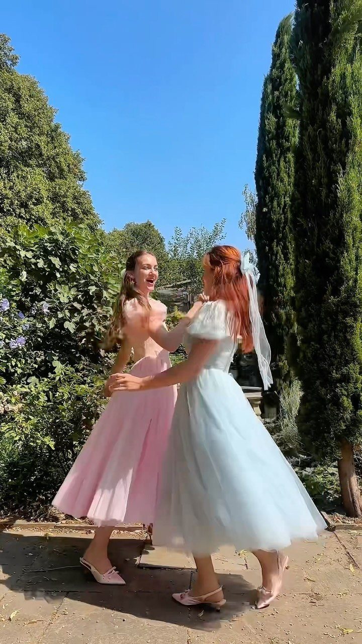 Two women playing in a garden wearing pink and light blue midi tulle dresses.