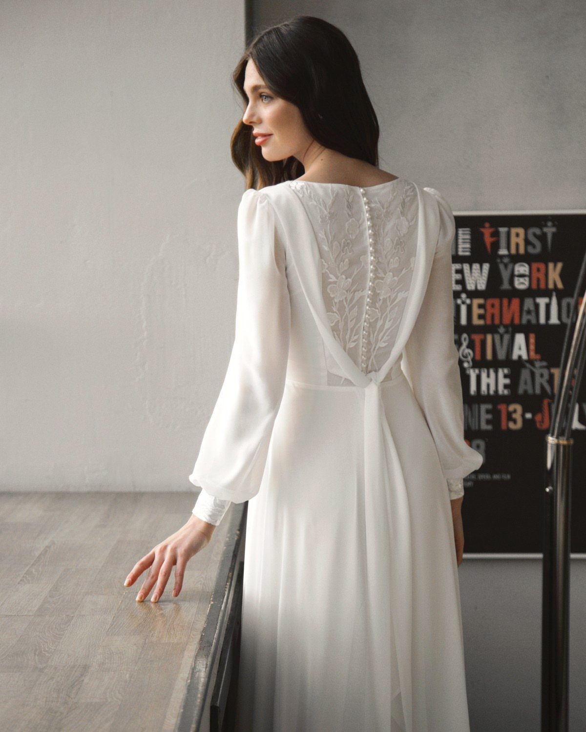 Woman in a white long-sleeved wedding dress with sheer chiffon sleeves and lace back detail.