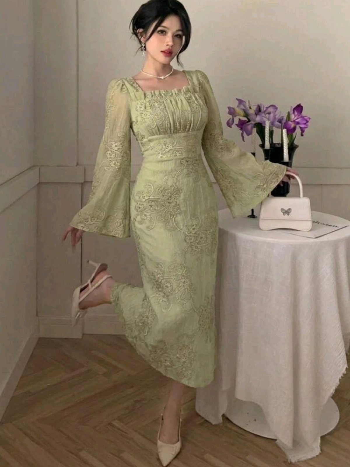 Woman posing in a light green lace midi dress with long bell sleeves.