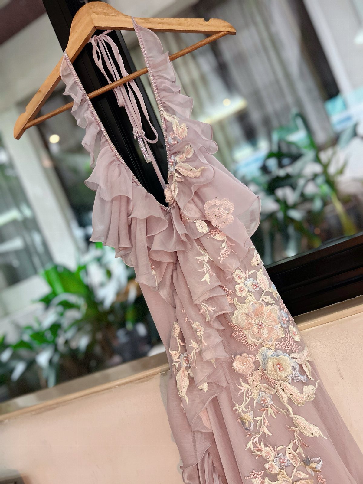 Mauve ruffled dress with floral embroidery hanging on a wooden hanger against a blurred background.