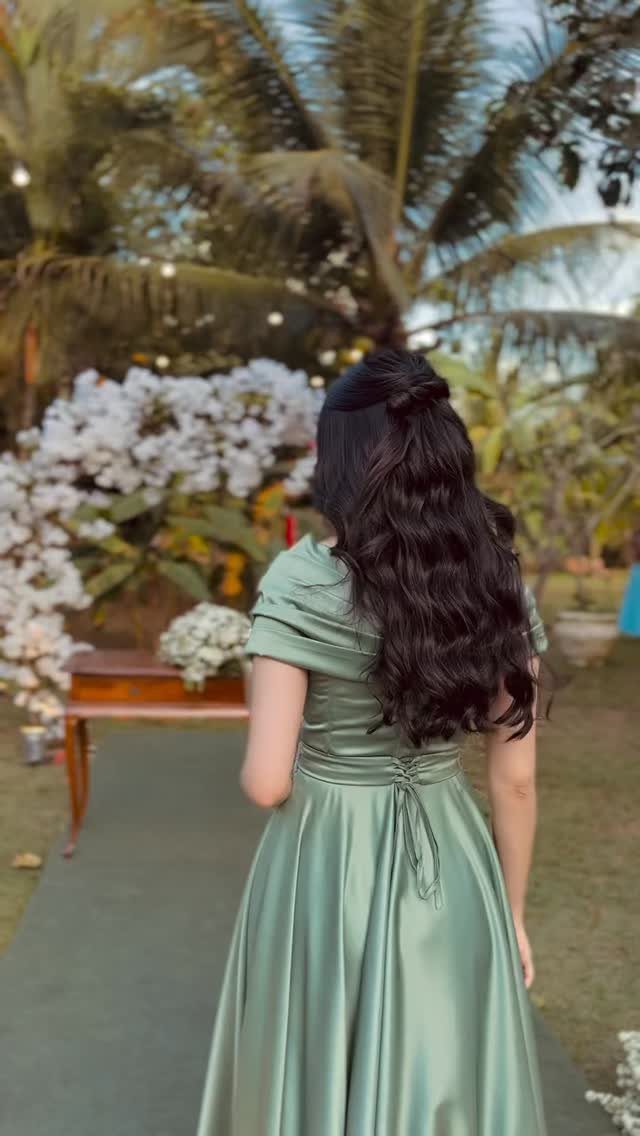 Woman in a sage green satin dress standing in a tropical garden with palm trees.