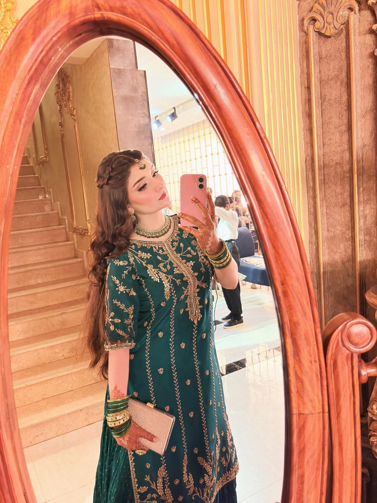 Woman in an ornate emerald green embroidered dress posing for a mirror selfie.