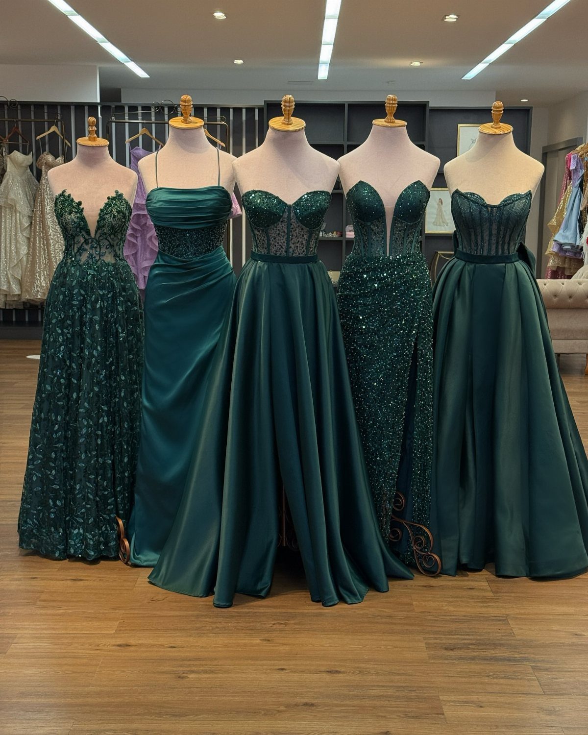 Five emerald green formal maxi dresses displayed on mannequins in a clothing boutique.