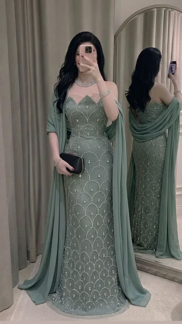 Woman posing in a sage green beaded formal gown with a matching sheer cape.