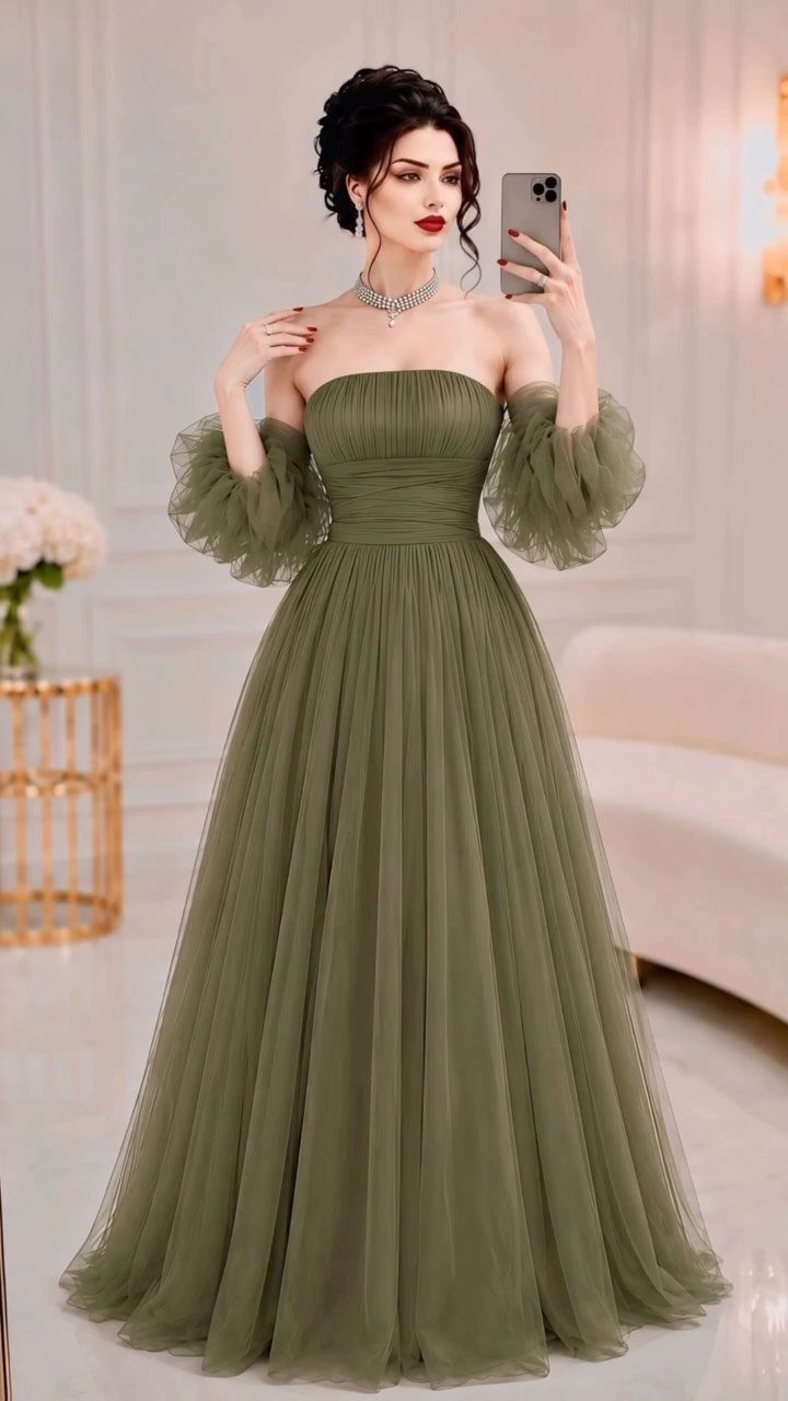 A woman posing in a strapless olive green tulle formal gown with voluminous puff sleeves.