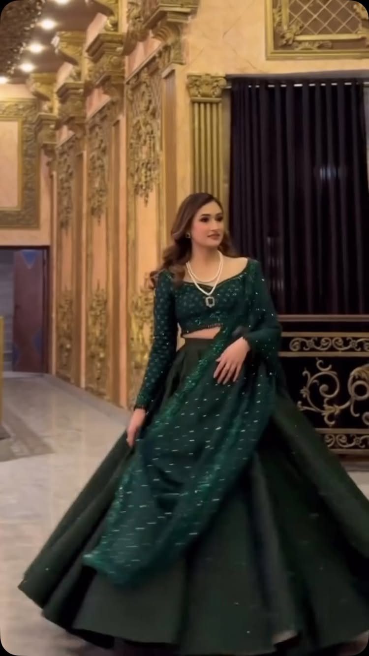 Woman in an emerald green embellished lehenga posing in a grand, gold-decorated hall.