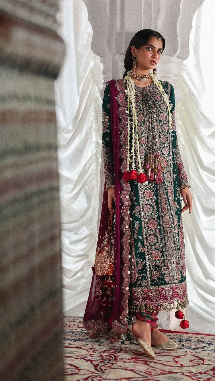 Woman wearing a dark green dress with intricate gold floral embroidery and traditional jewelry.
