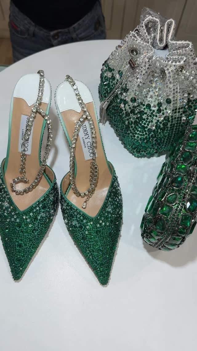Emerald green rhinestone high heels and a matching beaded clutch bag on a white surface.