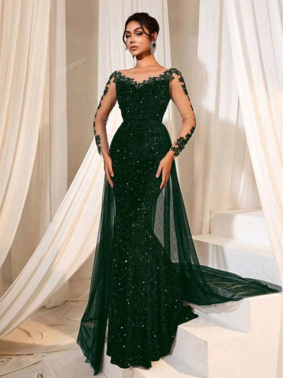 Woman wearing a dark green sequined evening gown with sheer sleeves and a long tulle train.