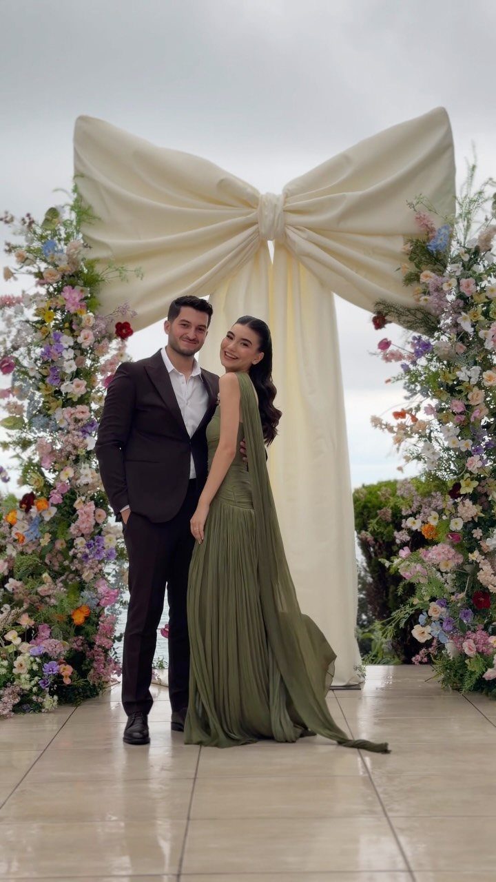A woman in a long olive green gown and a man in a dark suit posing outdoors.