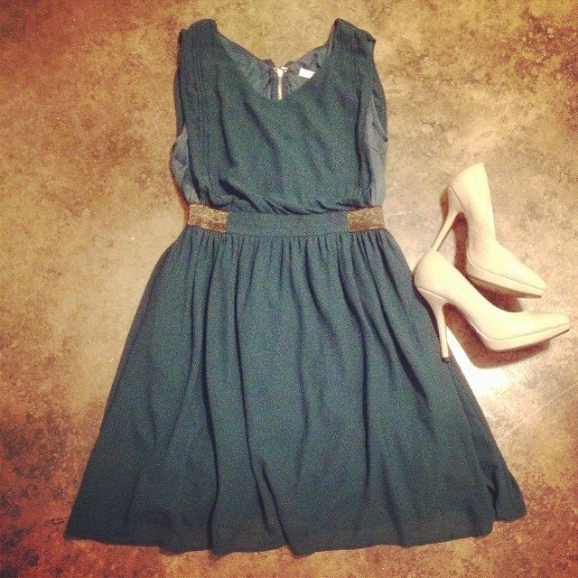 Teal sleeveless dress with a sparkly belt and white high heels on a brown floor.