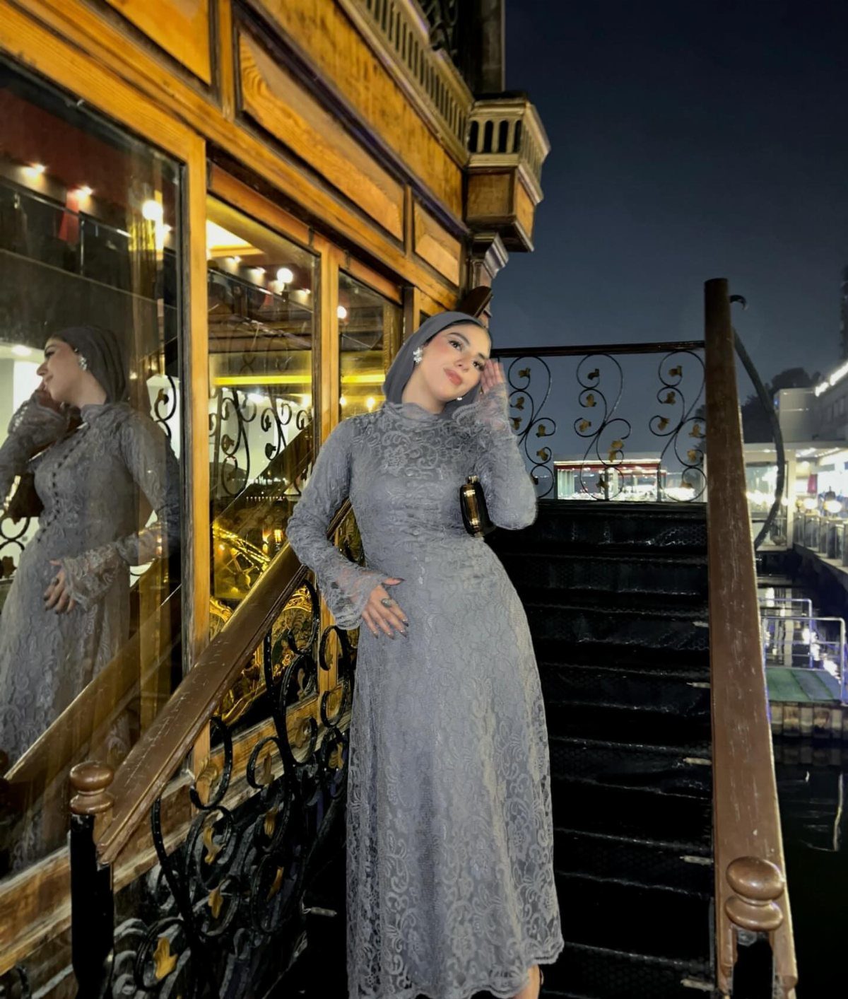 Woman in a grey lace maxi dress and headscarf posing on stairs at night.