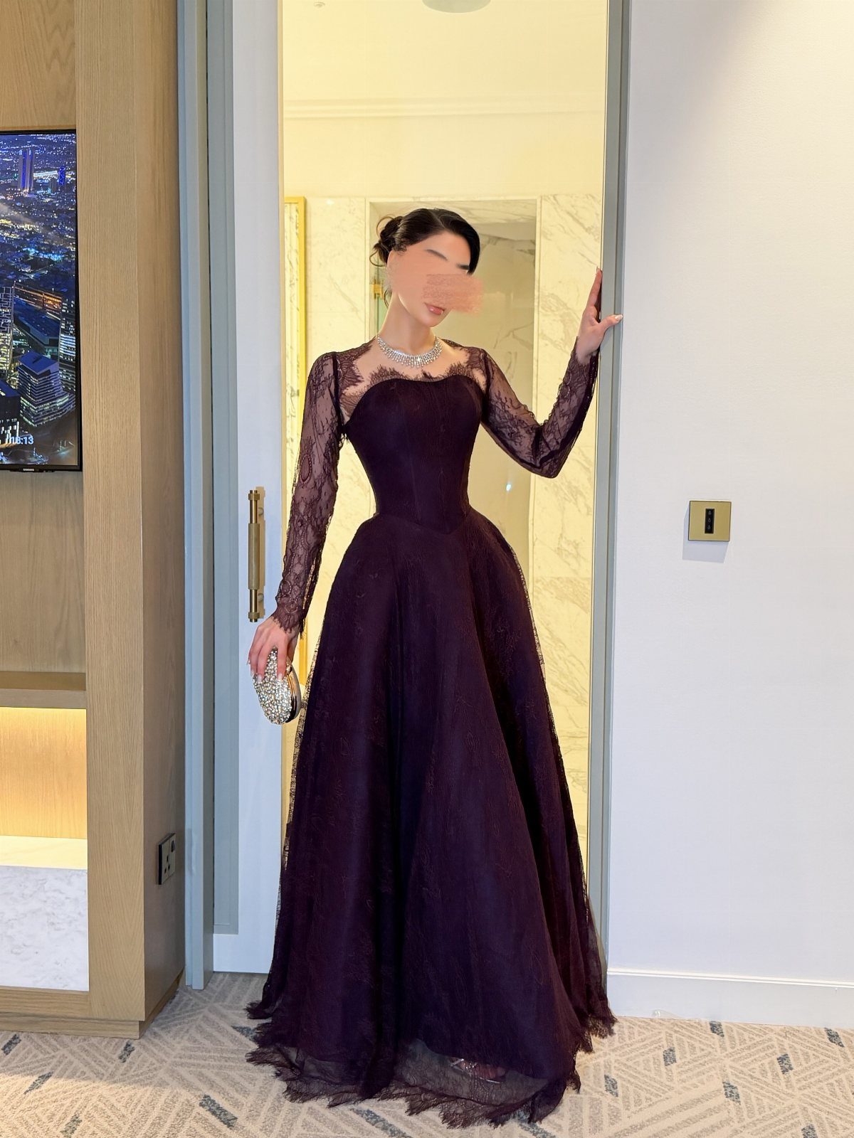 Woman wearing a dark purple lace corset maxi dress and holding a silver clutch.