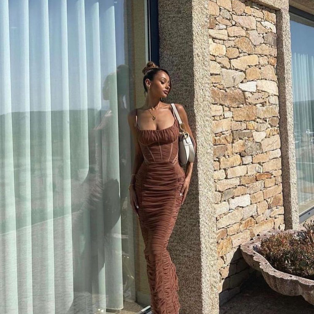 Woman in a rust-colored ruched corset maxi dress standing by a stone wall.