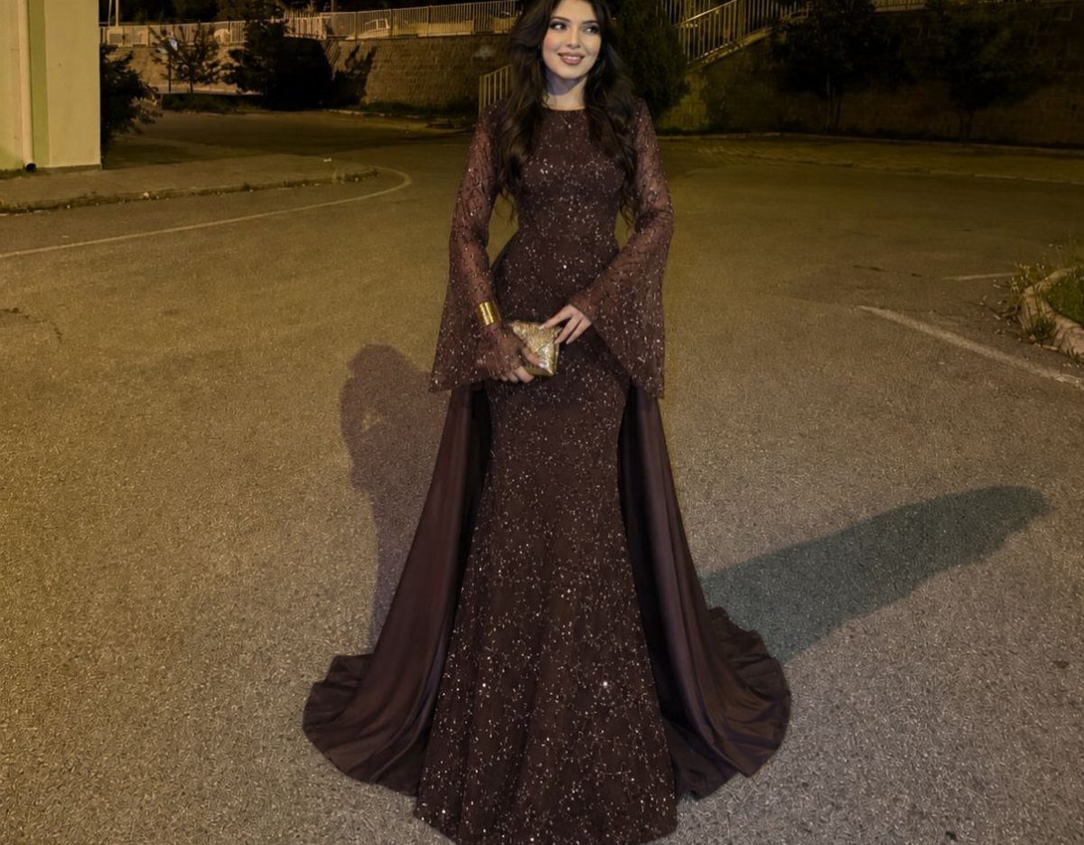 A woman in a shimmering dark burgundy embellished mermaid gown posing outdoors at night.