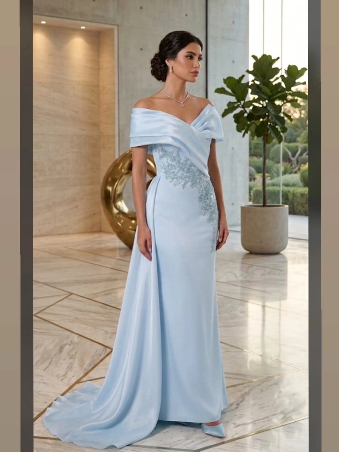 Woman wearing a light blue off-the-shoulder satin evening gown with floral embroidery standing in a modern room.