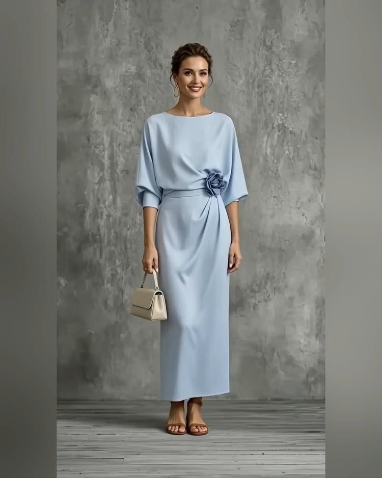 Woman in a light blue satin maxi dress holding a small cream handbag.