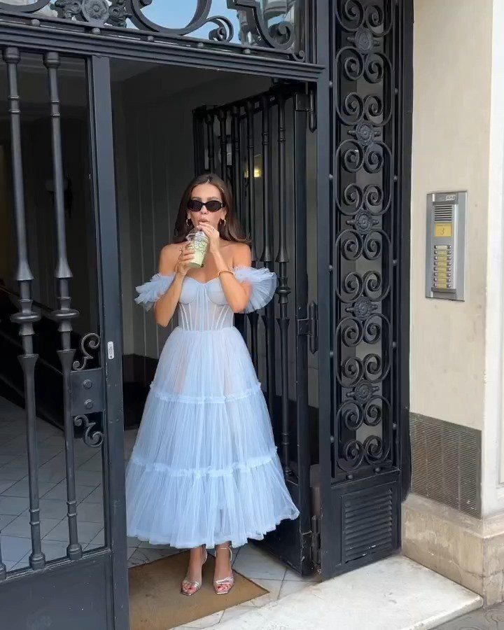Woman in a light blue tiered tulle dress standing by a black iron gate.