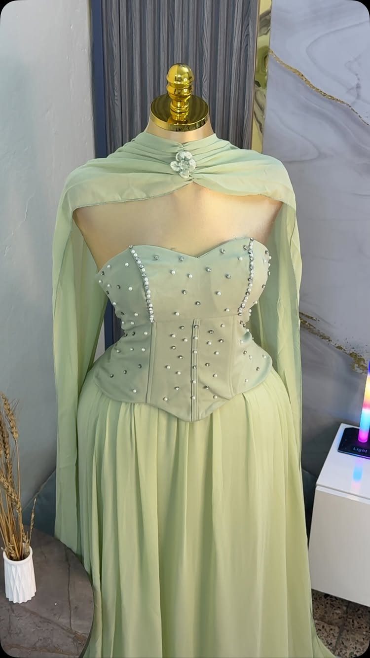 Light green formal gown with a pearl-embellished corset bodice and flowing chiffon skirt on a mannequin.
