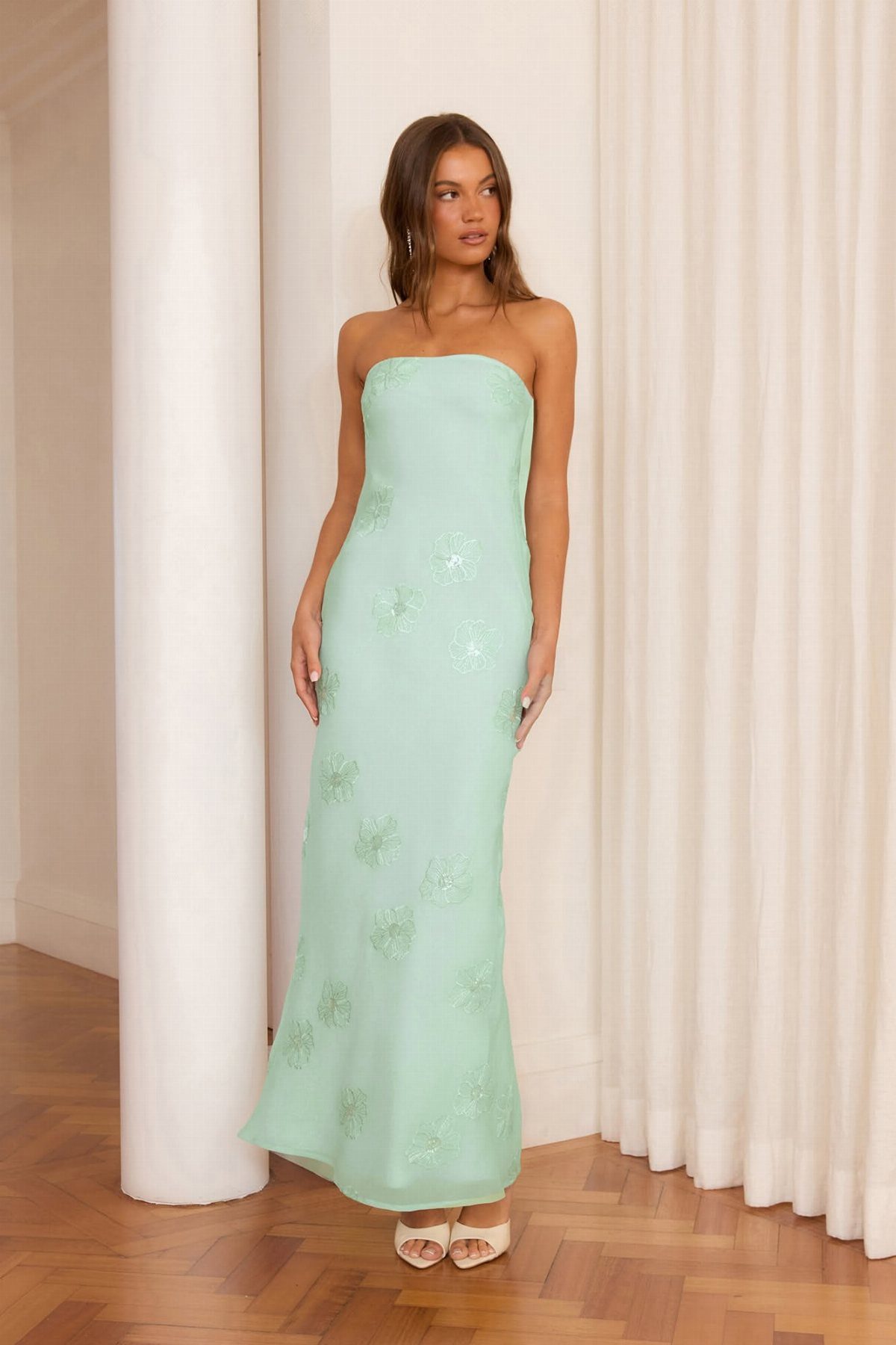 A woman wearing a strapless light green formal gown with floral embroidery standing indoors.