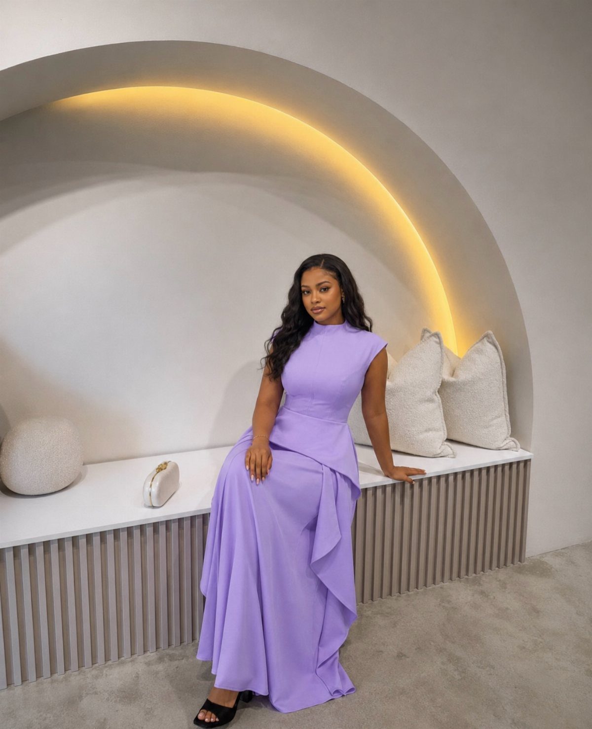 Woman in a sleeveless purple maxi dress sitting on a white bench in a modern room.